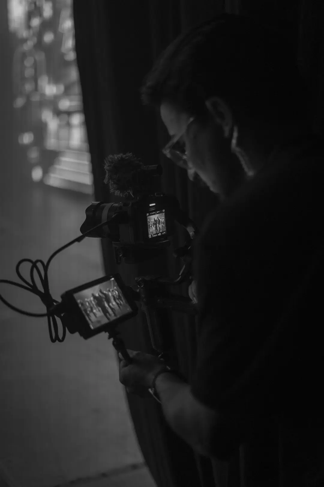 Cinegrafista na coxia acompanhando o palco pelo monitor, em preto e branco