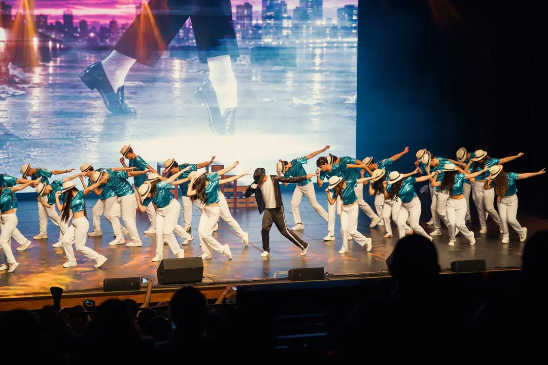 Turma inteira de chapéu em coreografia sincronizada diante do telão